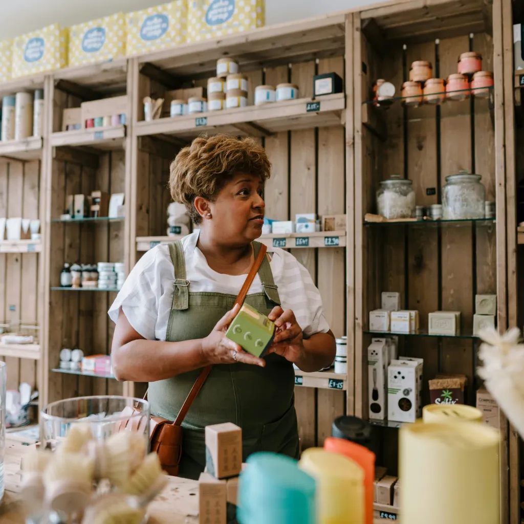 A shop owner holding a product among well-stocked wooden shelves in her store
