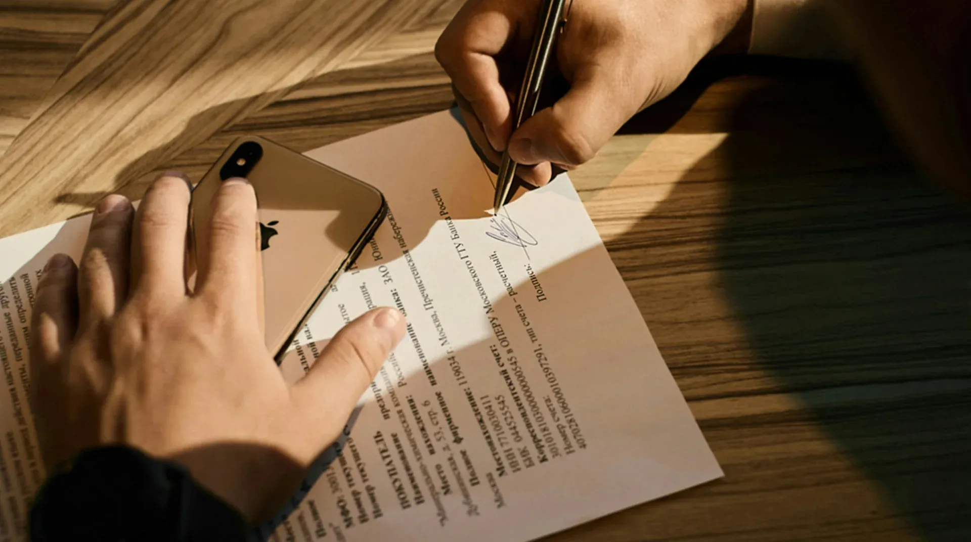 A hand signing a printed agreement on a wooden table